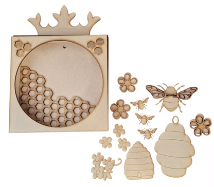 A wooden bee craft kit with various laser-cut wooden pieces including a beehive, honeycomb pattern, flowers, bees, and a crown, displayed on a clean white background.