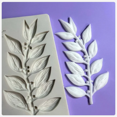 Silicone mold with leaf design next to a white leaf-shaped mold on a purple background
